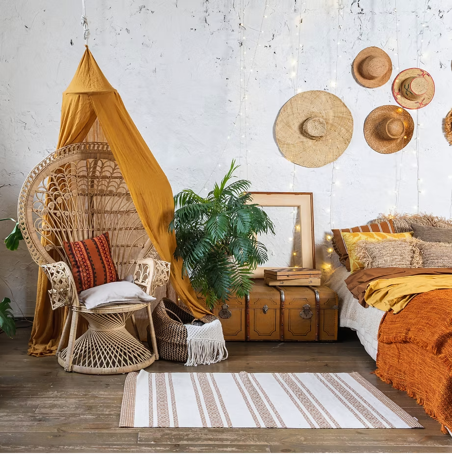Boho bedroom with a rattan peacock chair, mustard canopy and straw hats on the wall