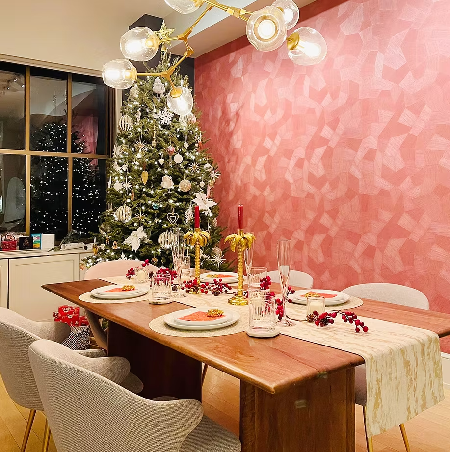 Festive dining room with a Christmas tree, pink textured wall and a set wooden table